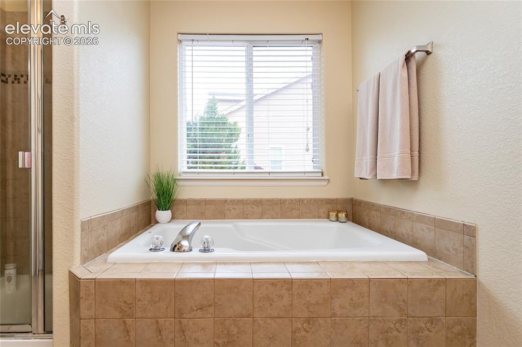 Image 19 of 49: Primary bathroom offers a soak-in tub with tile surround and tile flooring.