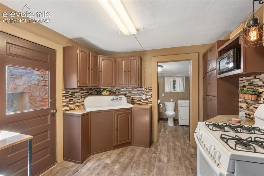 Image 16 of 40: Kitchen featuring wood-finish flooring, brown cabinetry, and a mosaic tile