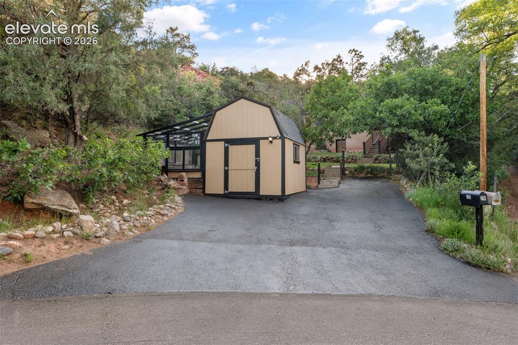 Image 32 of 40: Paved driveway with a detached gambrel-roof structure featuring double entr