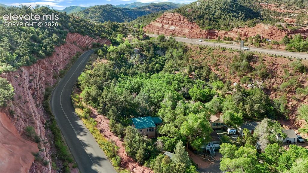 Image 38 of 40: Mountainous landscape featuring verdant trees, red rock formations, and a w