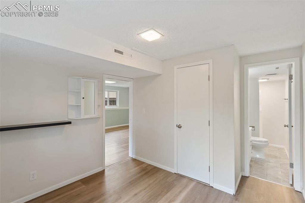 Image 19 of 25: Bedroom with light wood finished floors, a closet, an ensuite, and a textur