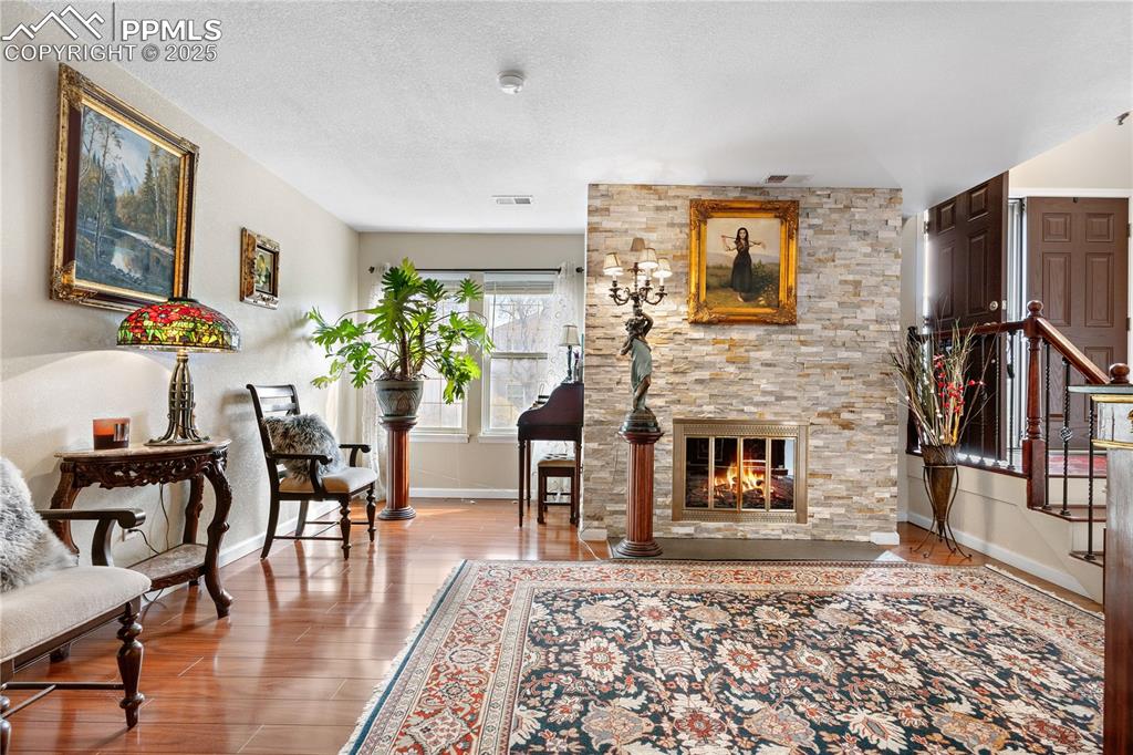Image 34 of 38: Living area with wood finished floors, a stone fireplace, and a textured ce