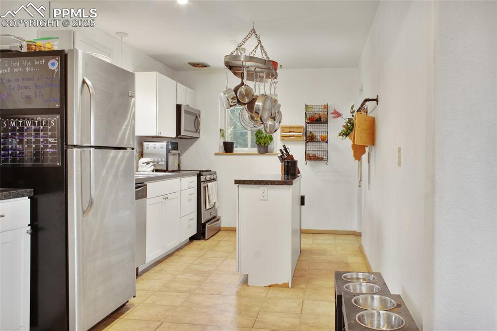 Image 7 of 28: Kitchen with dark countertops, stainless steel appliances, and white cabine