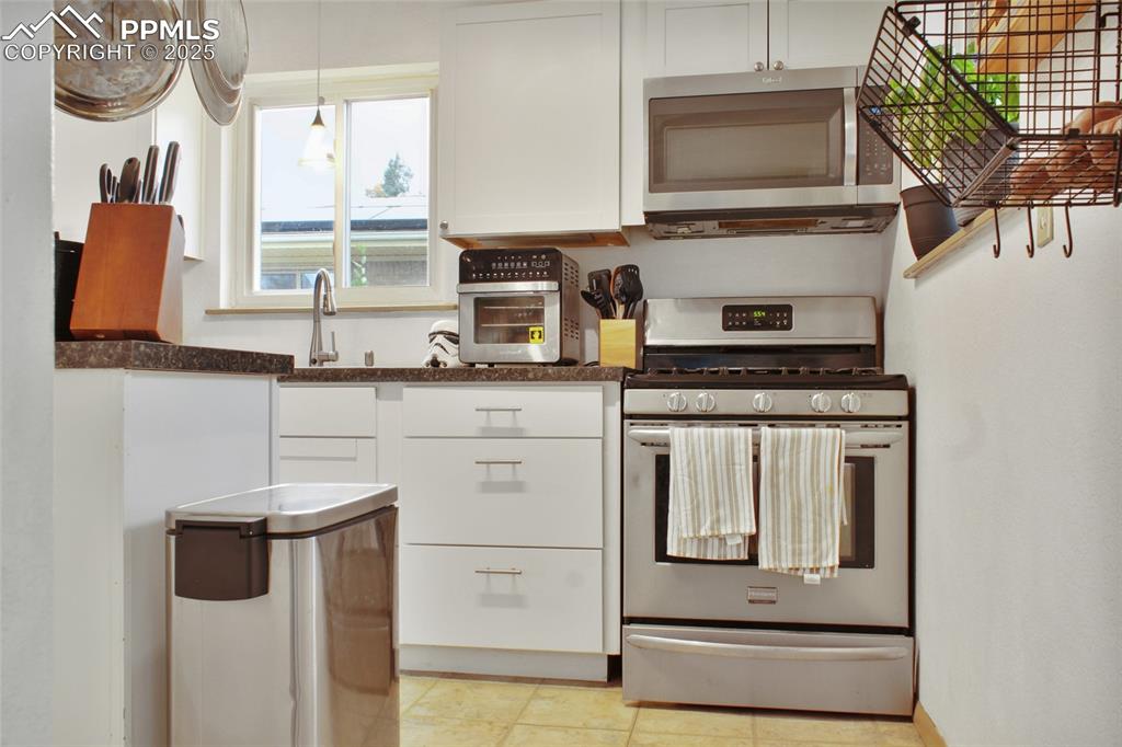 Image 8 of 28: Kitchen with white cabinets, stainless steel appliances, dark countertops,