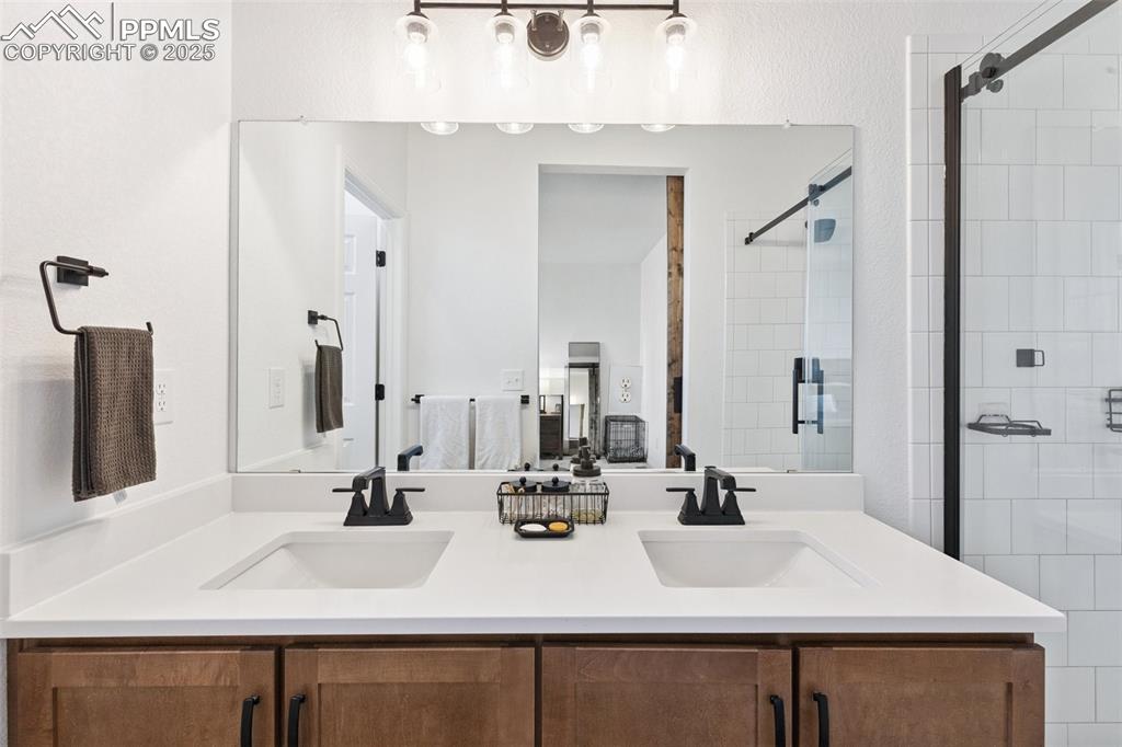 Image 24 of 46: View of the primary bathroom double vanity with quartz countertops, maple c