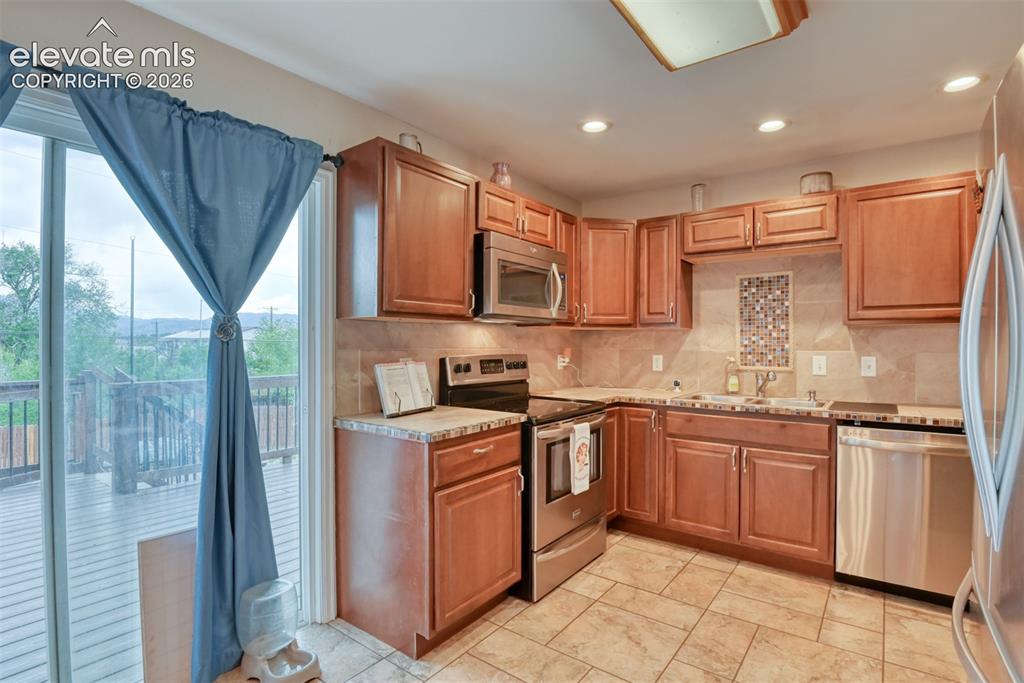 Image 10 of 46: Kitchen featuring wood cabinetry, stainless steel appliances, a tile backsp