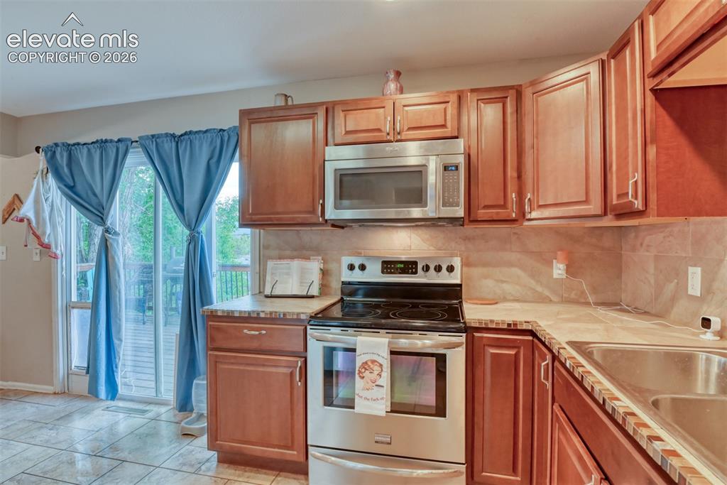 Image 12 of 46: Kitchen featuring wood cabinetry, stainless steel appliances, tile flooring