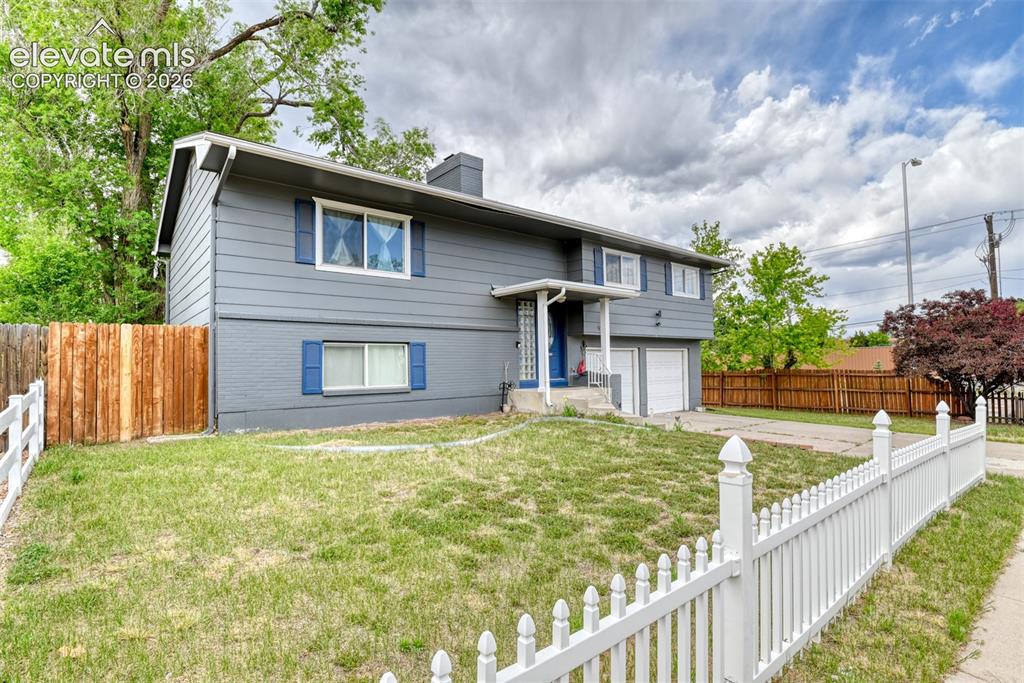 Image 2 of 46: Split-level residence featuring gray siding with blue window shutters, an a