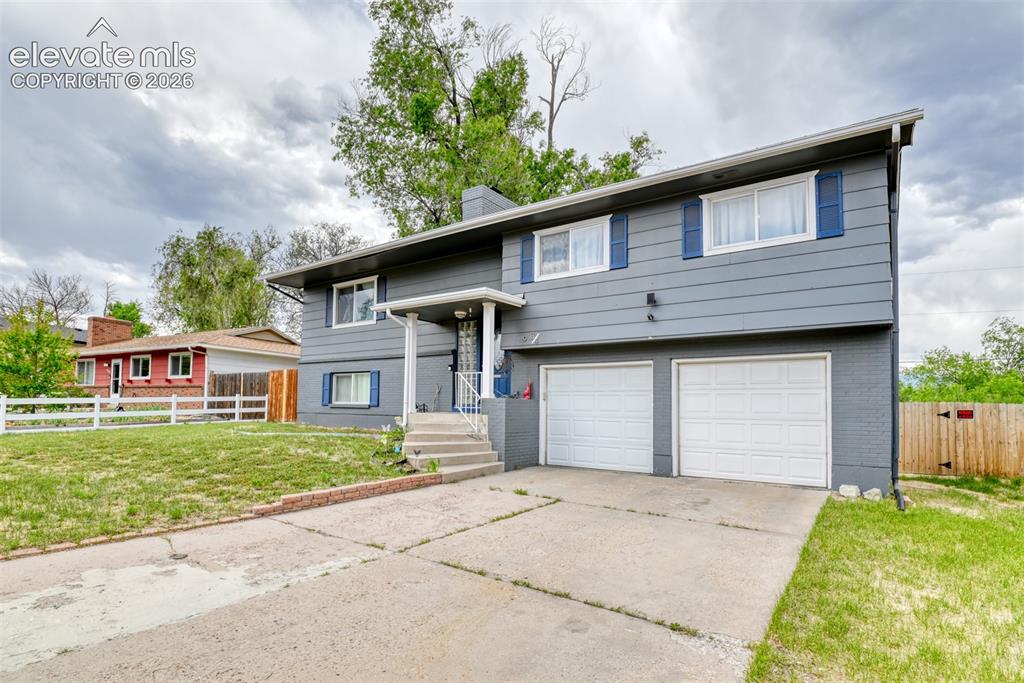 Image 3 of 46: Split-level residence featuring gray siding, blue window shutters, a covere