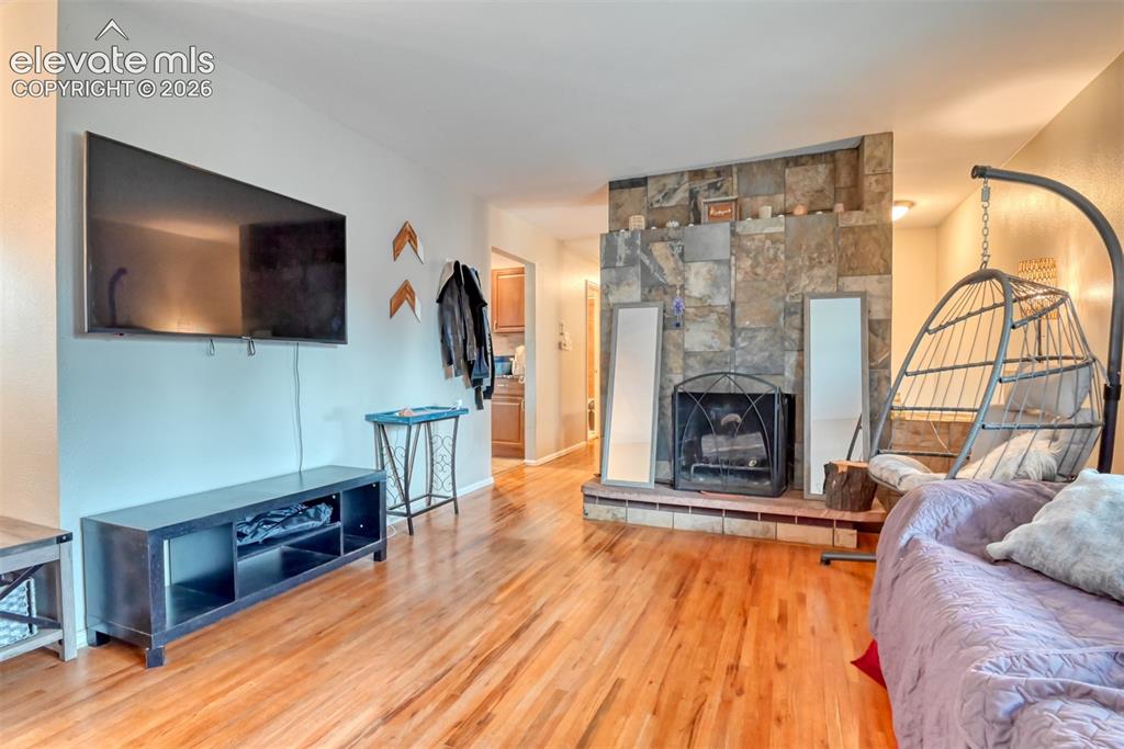 Image 5 of 46: Living area featuring wood-finish flooring, a stone-clad fireplace with a h