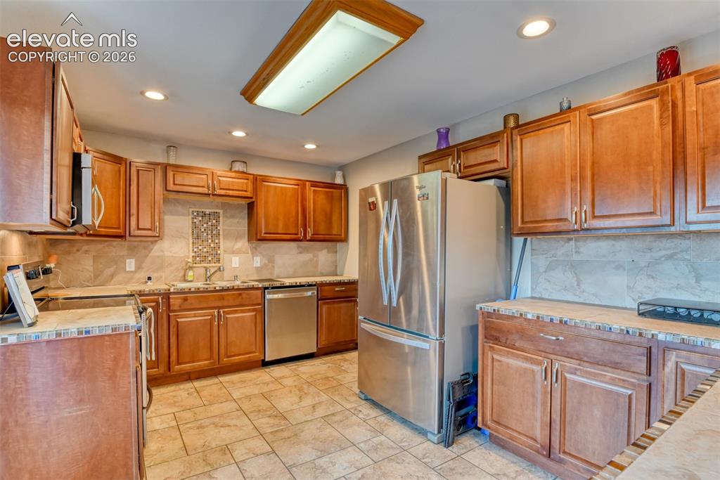 Image 7 of 46: Kitchen featuring wood-finish cabinetry, stainless steel appliances, tile b