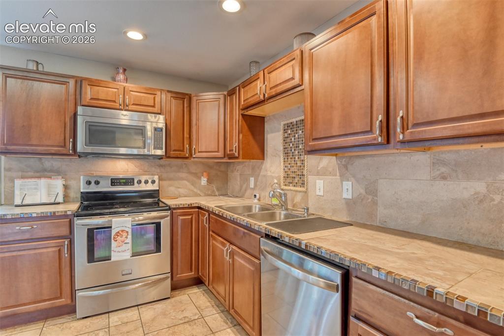 Image 9 of 46: Kitchen featuring wood cabinetry, stainless steel appliances, tile flooring