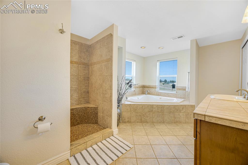 Image 31 of 42: This bathroom features a tiled shower with a built-in bench, a spacious cor