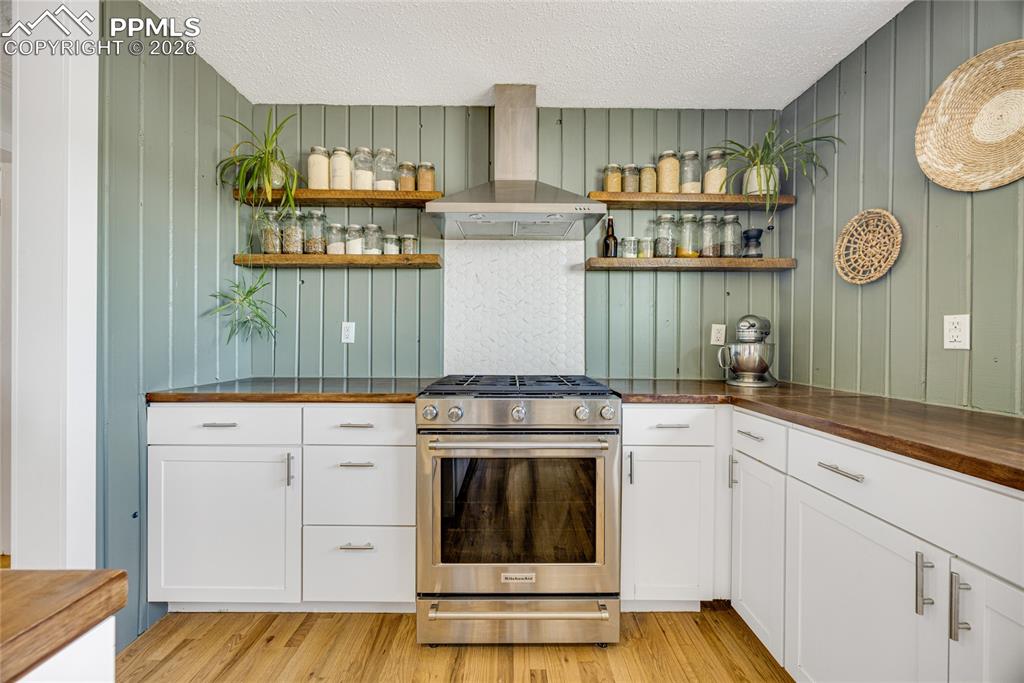Image 8 of 42: The kitchen features white cabinetry, wood countertops, and a stainless ste