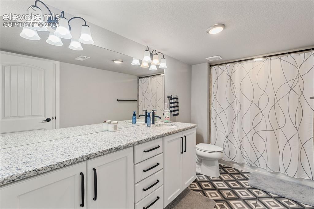 Image 39 of 44: Bathroom featuring a dual vanity with a speckled countertop, white cabinetr