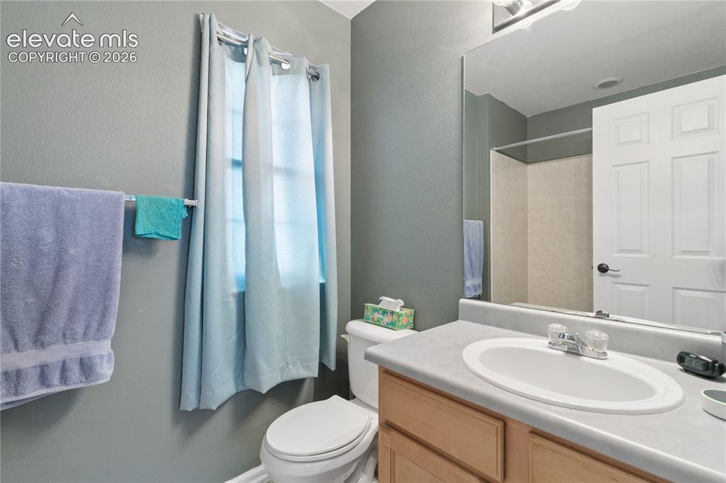 Image 15 of 35: Vanity with an oval sink and chrome faucet, wood-finish cabinetry, and a fu