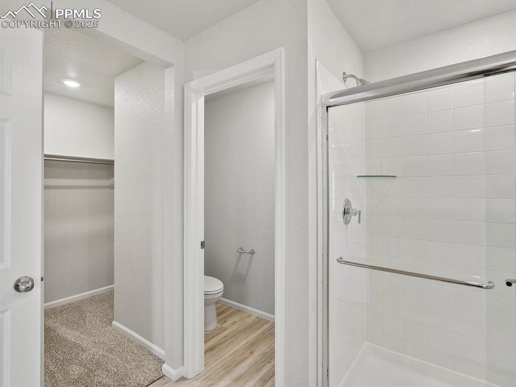 Image 14 of 22: Bathroom with a shower stall, a walk in closet, and wood finished floors