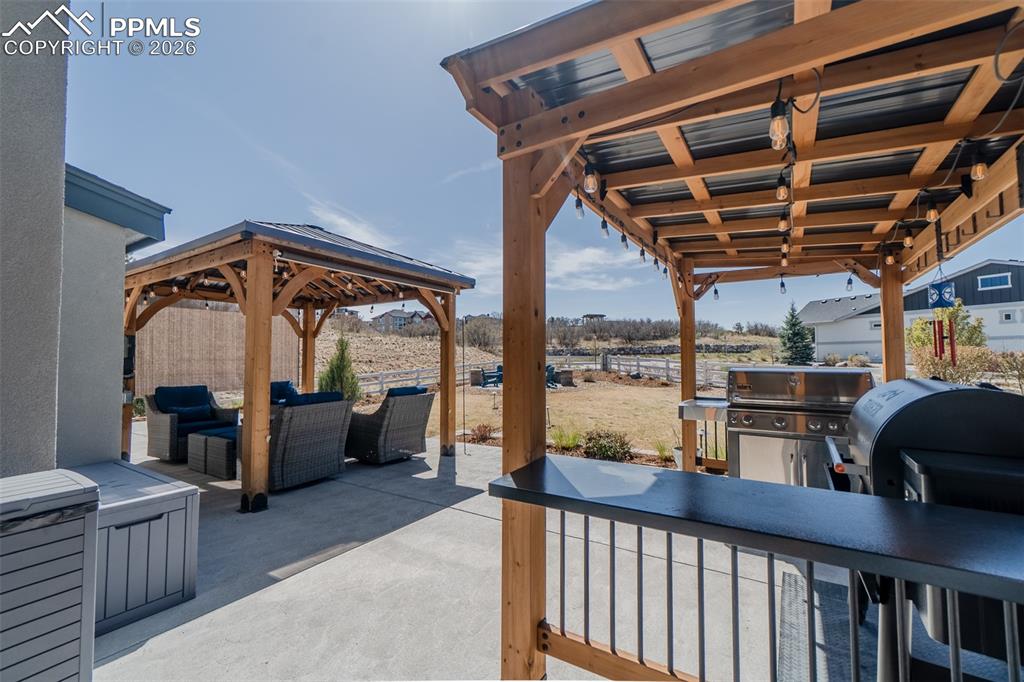 Image 19 of 49: Expansive concrete patio featuring a wood-beam pergola with string lighting