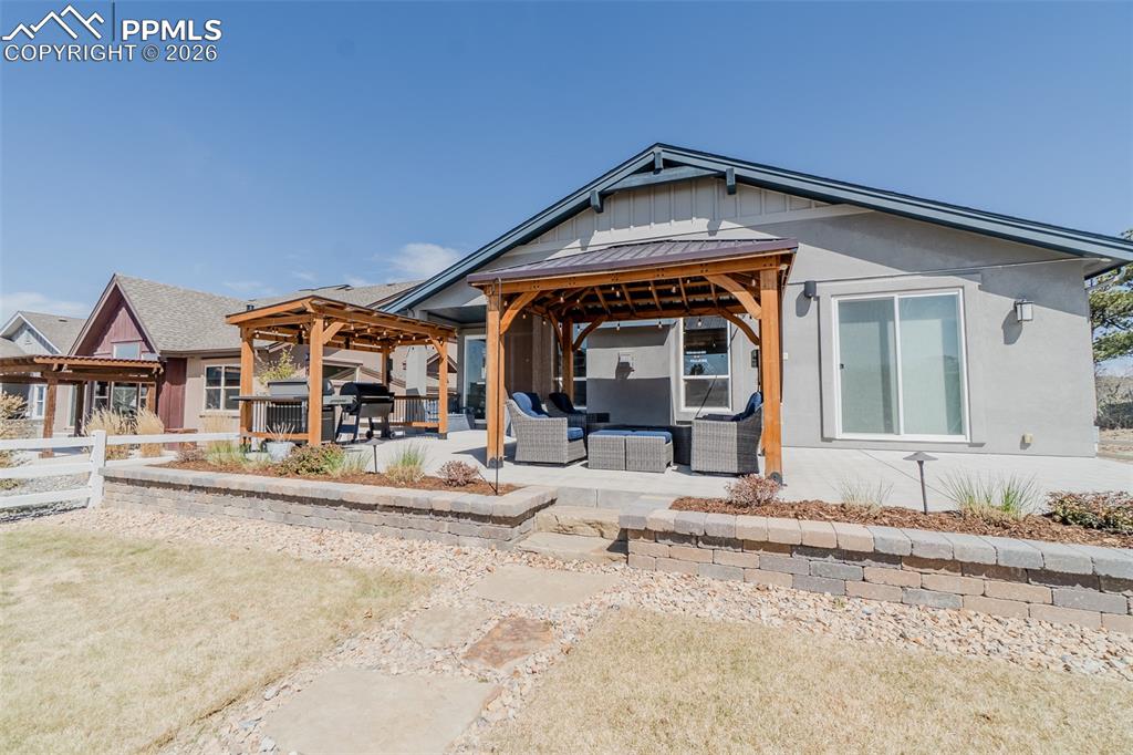 Image 21 of 49: Back patio featuring two wooden pergolas with dark metal roofs, a concrete 