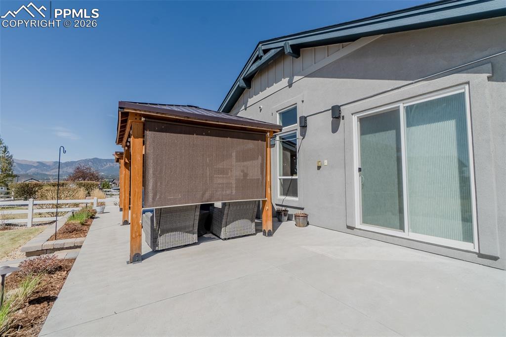 Image 26 of 49: Expansive concrete patio featuring a wood-beam pergola with a metal roof an
