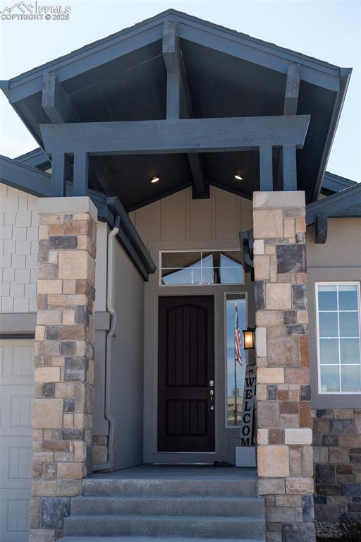 Image 3 of 49: Entryway featuring a dark wood front door, stone veneer columns, and expose