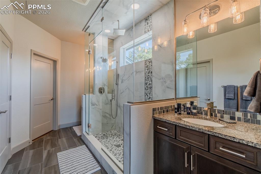 Image 30 of 49: Bathroom featuring an expansive glass-enclosed shower with pebble-tiled flo