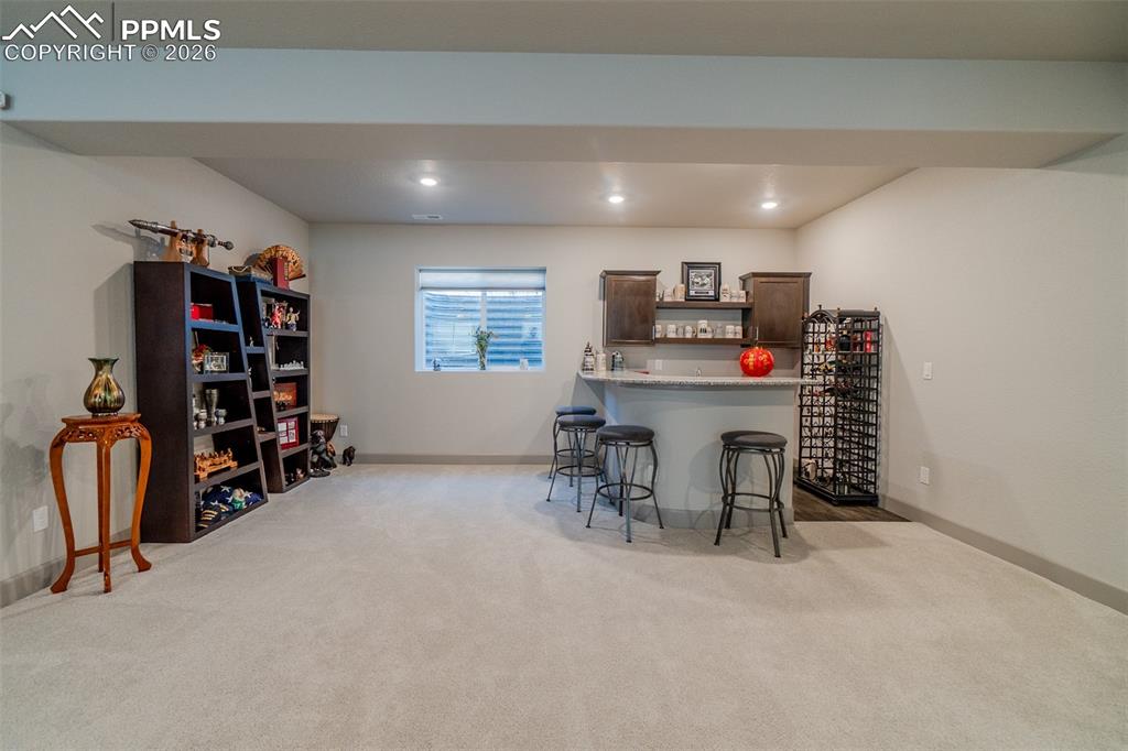 Image 38 of 49: Lower-level recreation space featuring a built-in wet bar with dark wood ca