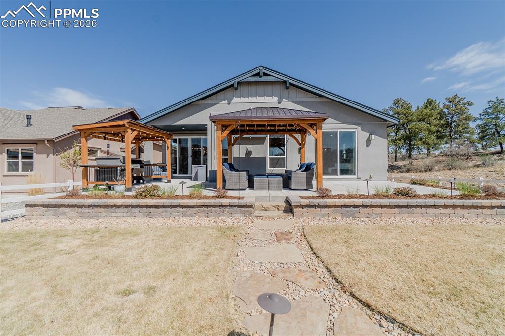 Image 45 of 49: Spacious backyard featuring multiple patio areas with pergolas, a stone ret