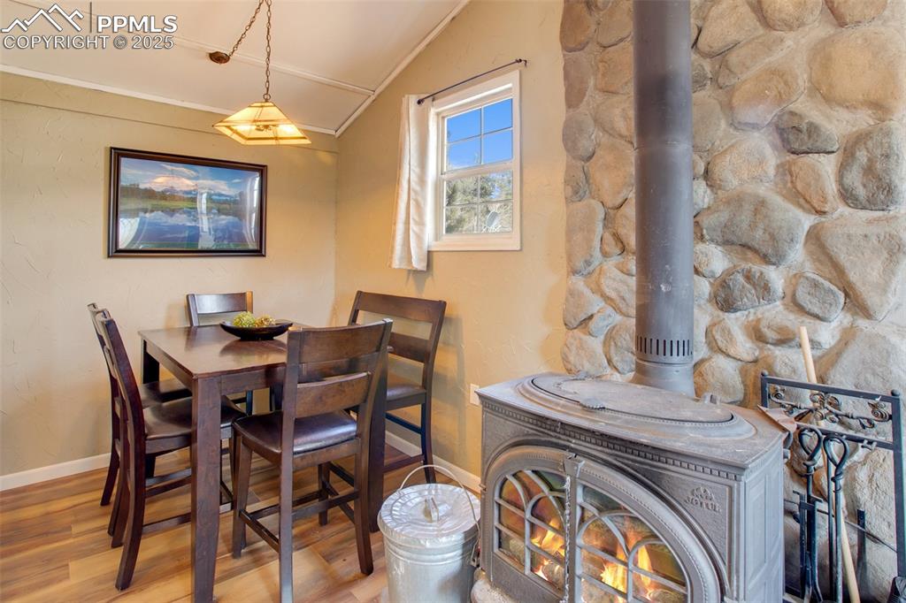 Image 17 of 36: Dining space with a wood stove, wood finished floors, and vaulted ceiling