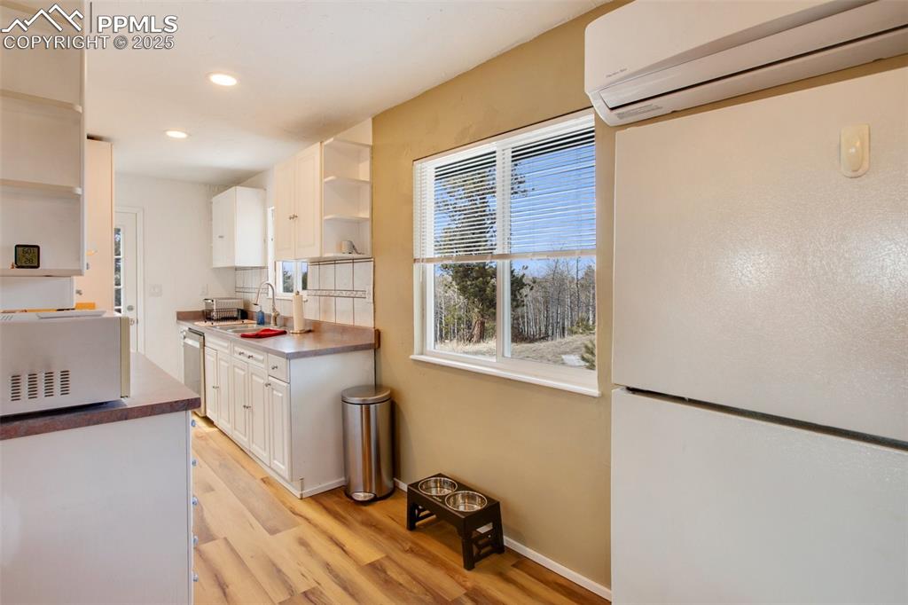 Image 18 of 36: Kitchen featuring open shelves, an AC wall unit, white microwave, white cab