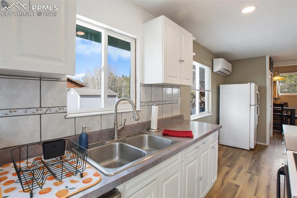 Image 23 of 36: Kitchen featuring freestanding refrigerator, white cabinets, decorative bac