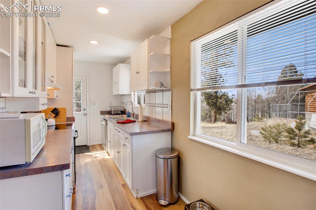 Image 6 of 36: Kitchen featuring white cabinetry, white appliances, dark countertops, ligh