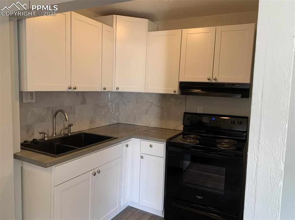 Image 18 of 49: Kitchen with black electric range oven, under cabinet range hood, and white