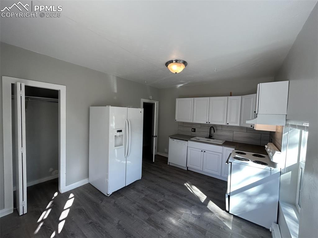 Image 26 of 49: Kitchen with white appliances, white cabinetry, dark wood-type flooring, ta