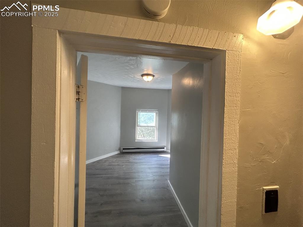 Image 28 of 49: Hallway with dark wood-style floors, a textured wall, and a baseboard radia