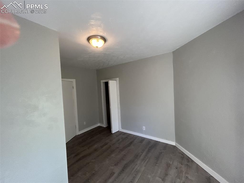 Image 29 of 49: Unfurnished room with dark wood-style floors and baseboards