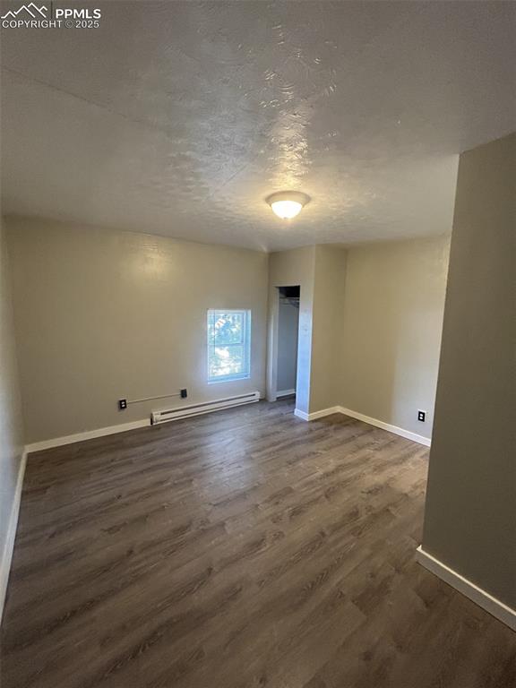 Image 30 of 49: Empty room with a textured ceiling, baseboard heating, and dark wood-type f
