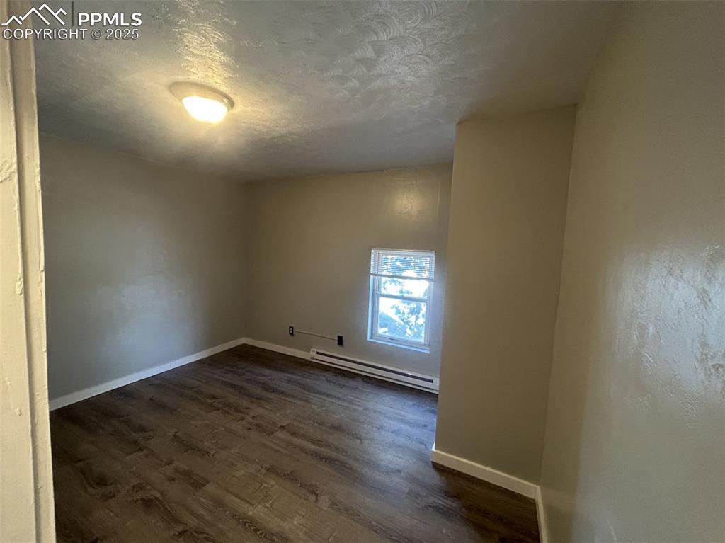 Image 31 of 49: Spare room with dark wood finished floors, a textured ceiling, and a basebo