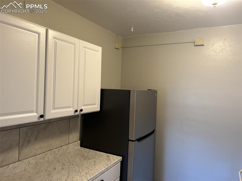 Image 39 of 49: Kitchen featuring white cabinetry, freestanding refrigerator, and backsplas