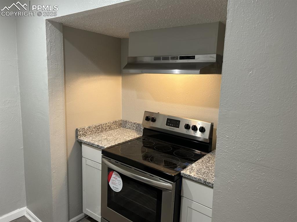 Image 4 of 49: Kitchen with a textured wall, stainless steel electric stove, white cabinet