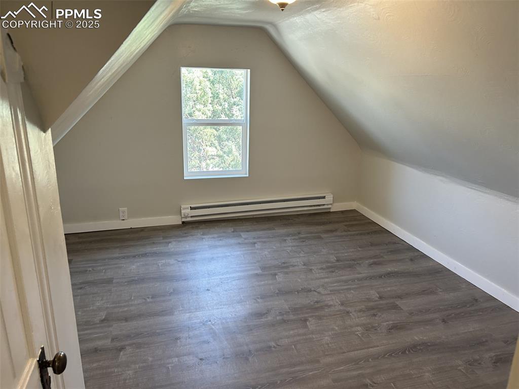 Image 46 of 49: Bonus room with baseboard heating, dark wood-style floors, and lofted ceili