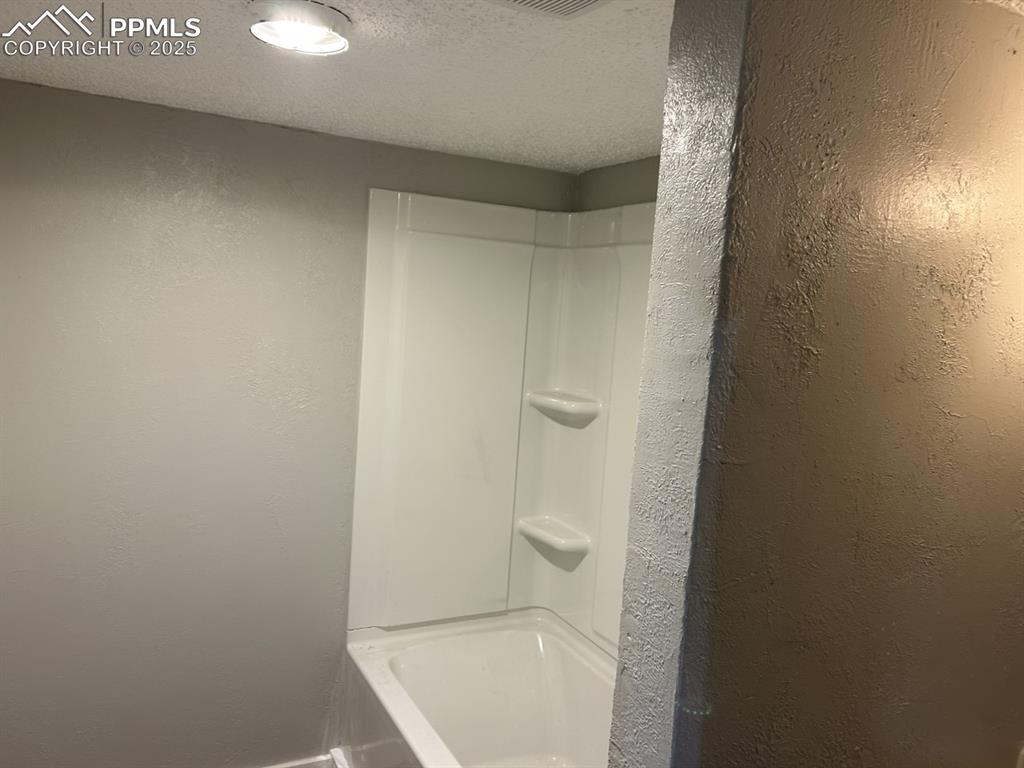 Image 5 of 49: Full bath with a textured ceiling, a textured wall, and shower / washtub co