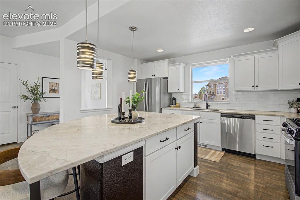 Image 12 of 35: Kitchen featuring a large curved island with a light-toned countertop, pend
