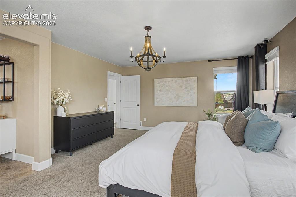 Image 20 of 35: Carpeted bedroom featuring a rustic-style chandelier, neutral wall tones