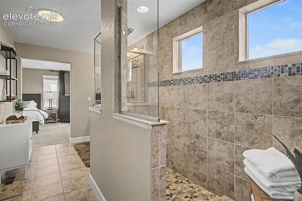 Image 22 of 35: Spacious shower enclosure with floor-to-ceiling stone-look tile, glass part