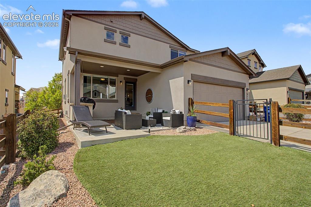 Image 32 of 35: Rear exterior featuring a covered patio, artificial turf lawn, and a two-ca
