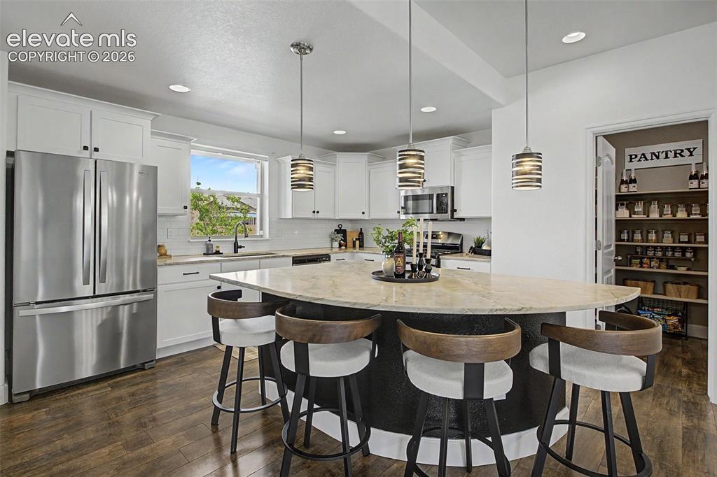 Image 5 of 35: Contemporary kitchen featuring an oversized island wi white cabinetry, stai