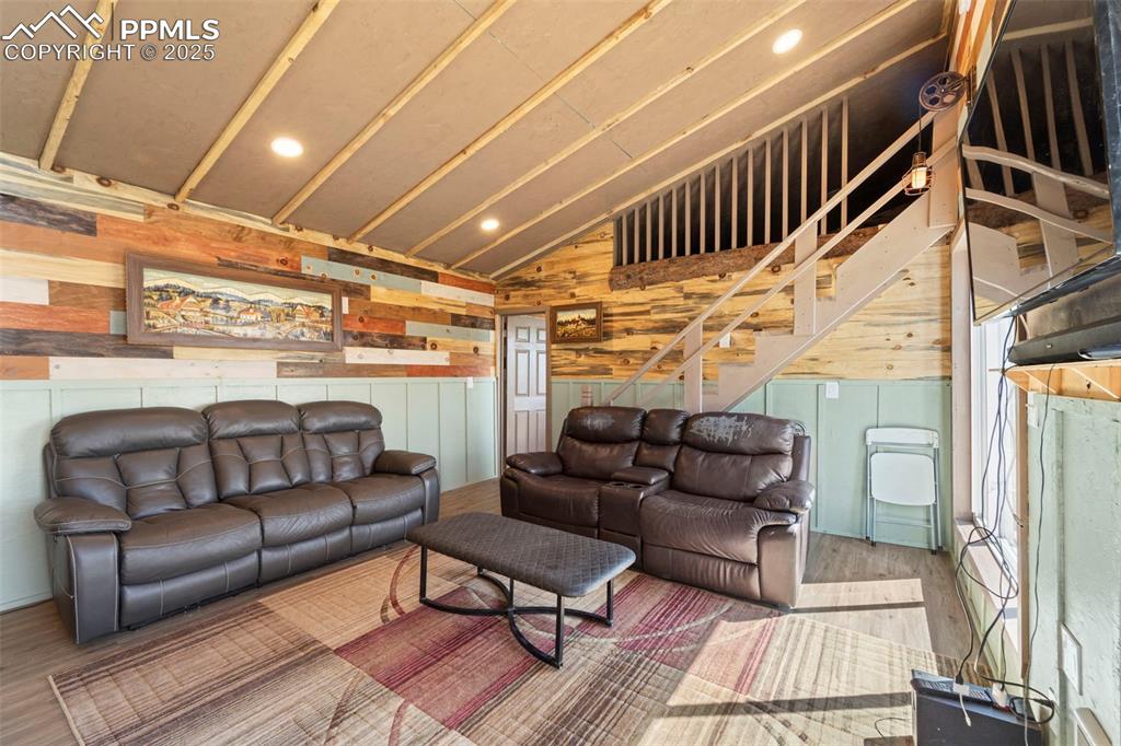 Image 23 of 35: Living room featuring vaulted ceiling, wood finished floors, wooden walls, 