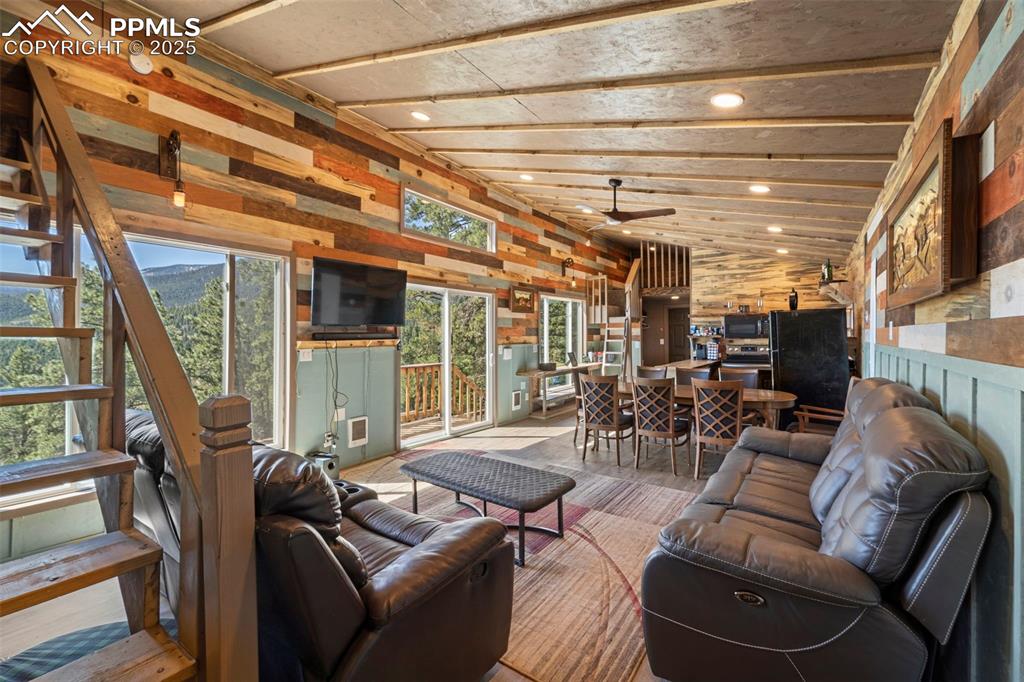 Image 29 of 35: Living area with lofted ceiling, a ceiling fan, stairs, and wooden walls