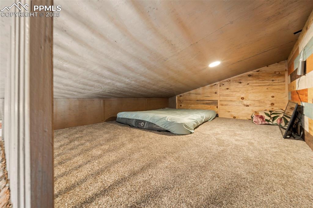 Image 34 of 35: Loft area/ bedroom featuring vaulted ceiling, wood ceiling, wooden walls, a